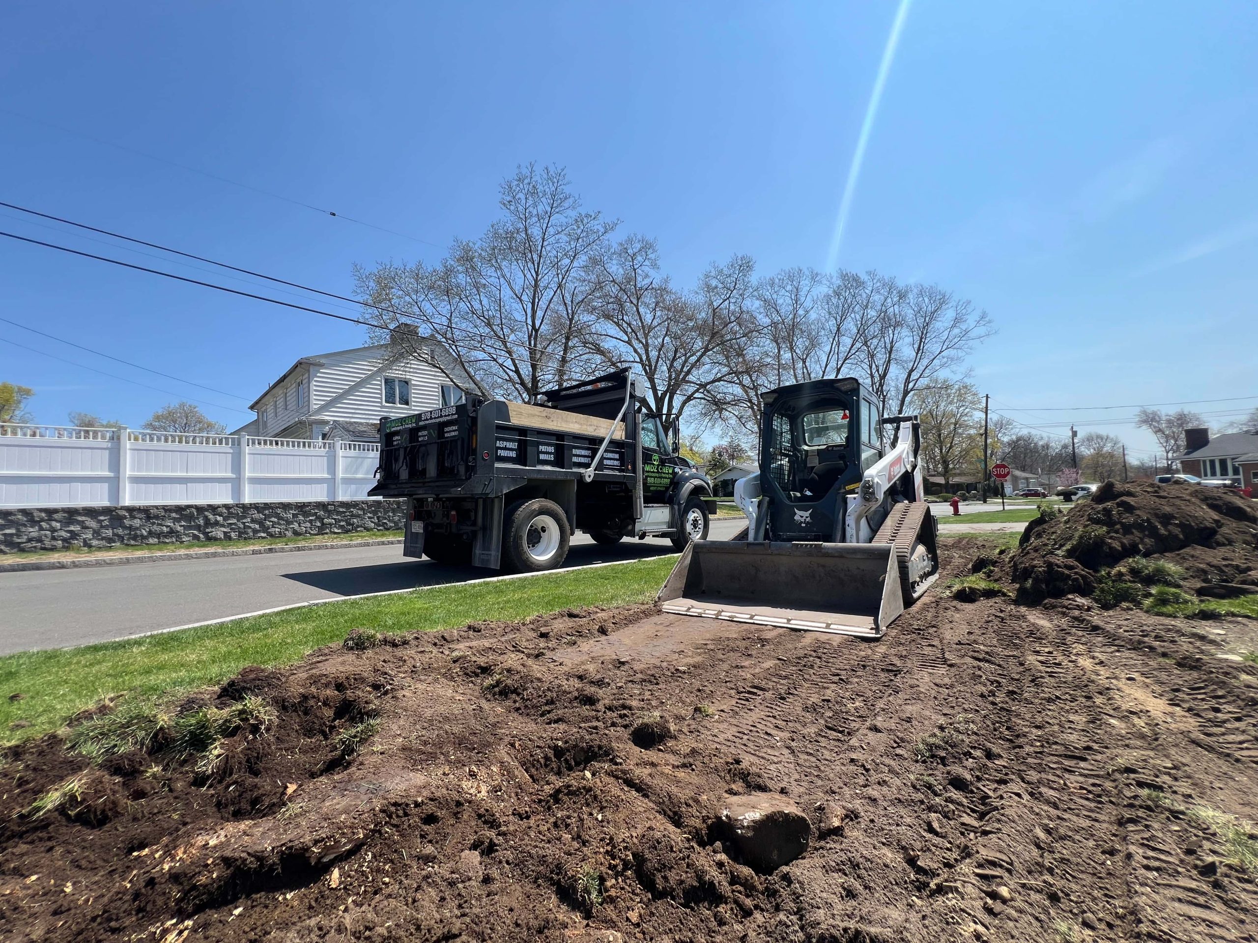 Professional paving contractor performing site preparation and grading work with skid steer and dump truck before asphalt paving