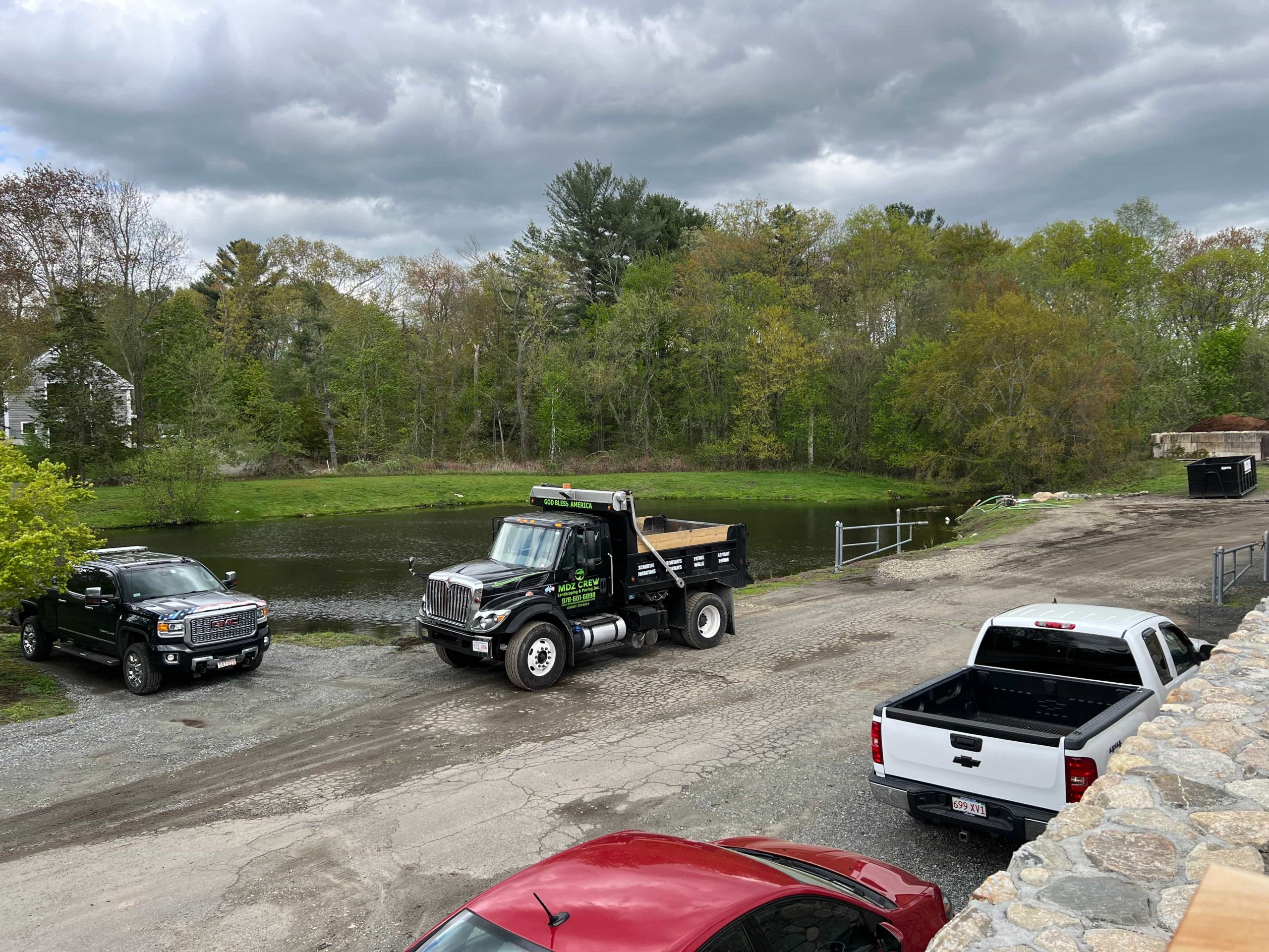 Dump truck and paving contractor vehicles at residential job site showing asphalt paving and driveway paving services by MDZ Crew Landscaping.
