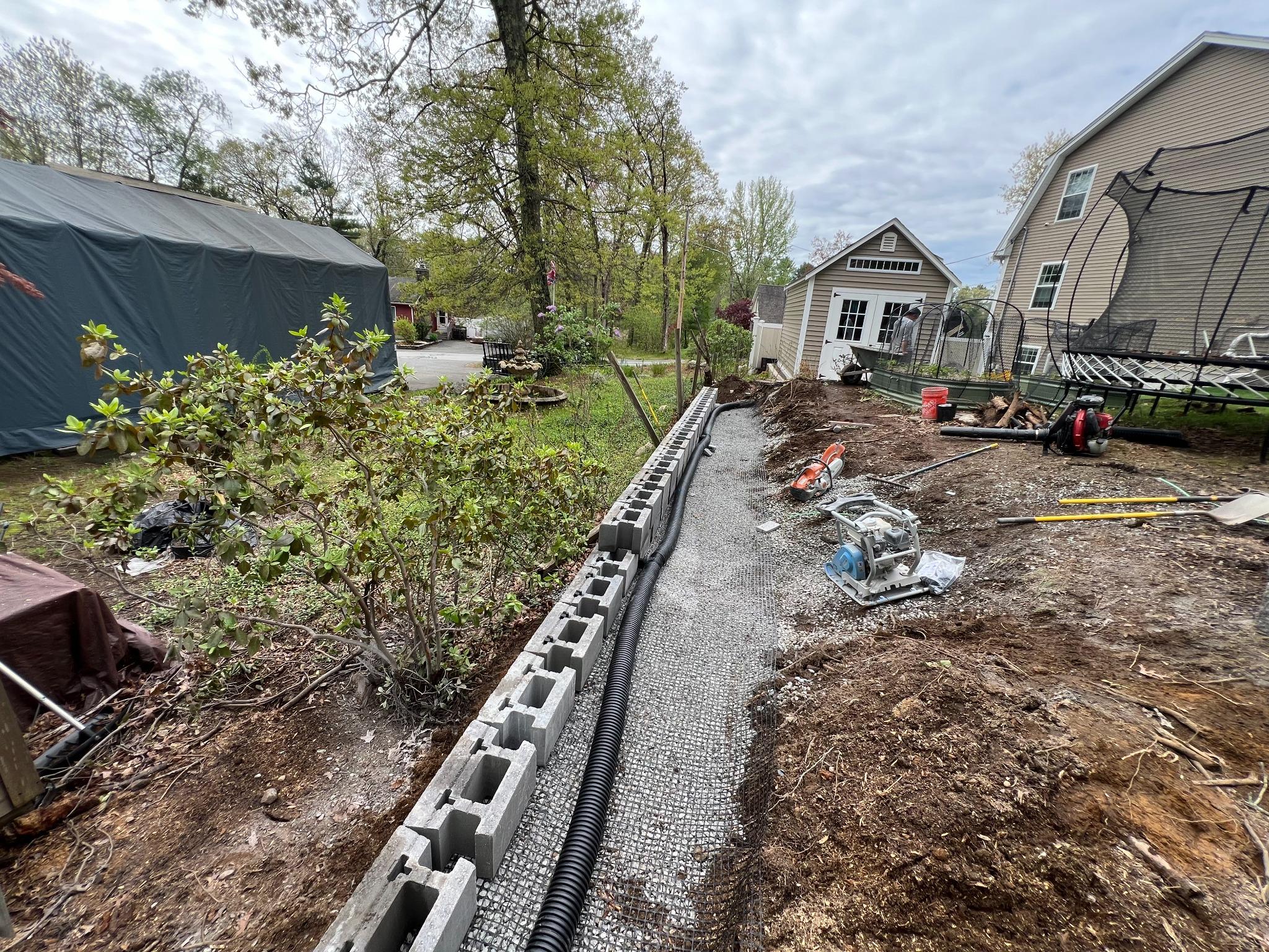 landscape drainage system installation project Residential landscape drainage system installation with gravel base and retaining wall blocks