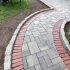 Curved paver walkway with brick border and natural stone edging beside landscaped planting beds