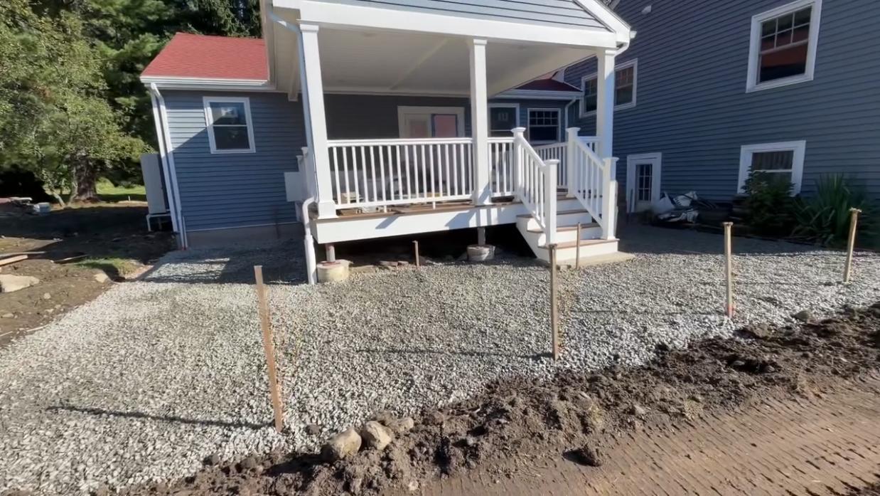 Paver patio base preparation with compacted stone aggregate around a residential porch